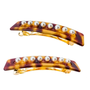 Detail of two tortoise shell hair clips with white pearl inlay and gold metal clip