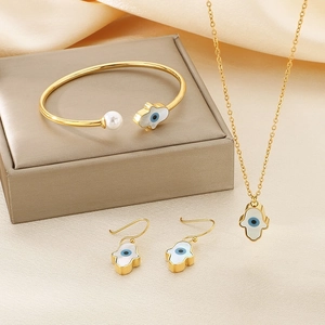 Hamsa Hand gold jewelry set with white shell and blue eye on beige silk backdrop
