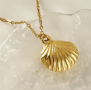 Detailed close-up of a gold seashell pendant on a delicate chain over glass