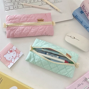 Close-up of quilted nylon pencil cases in pink and mint green colors on a desk