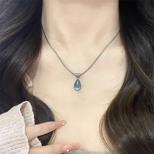 Detail of silver snake chain with blue teardrop pendant worn on model neck