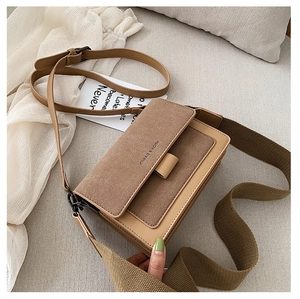 Close-up of brown suede patchwork crossbody bag with wide strap and brand logo detail