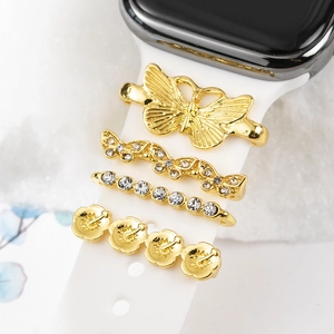 Macro view of golden butterfly and rhinestone charms on a white silicone watch band