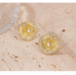 Macro detail of gold lotus leaf earrings with brushed texture and sparkling zircon stones