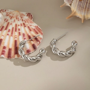 Dettaglio ravvicinato di orecchini geometrici a spirale in argento su superficie beige
