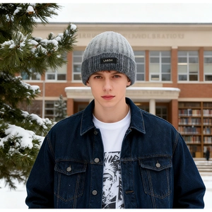 Close-up of grey knit beanie with brand label against a snowy winter forest background