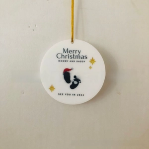 Close-up of ceramic Christmas ornament for new parents with baby footprints and 2024 text