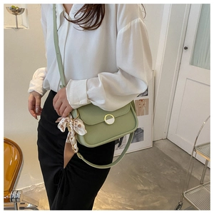 Close-up of a light green crossbody bag with an elegant floral scarf on the shoulder strap
