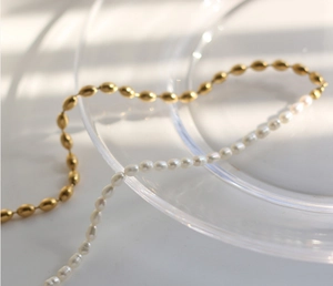 Detail of mechanical splice pearl necklace with gold plated beads on a glass plate