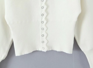 Detail des weißen Strickcardigans mit Wellensaum und metallischen Knöpfen