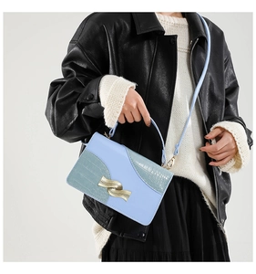 Detail of light blue crossbody bag featuring faux crocodile texture and gold wavy buckle