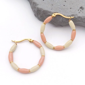 Macro detail of gold-plated bamboo hoop earrings with pink enamel beads on white stone