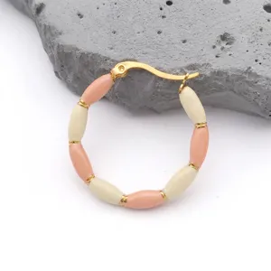 Macro detail of gold-plated bamboo hoop earrings with pink enamel beads on white stone