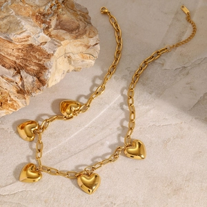 Gold stainless steel chain necklace with five puffy heart pendants on textured background