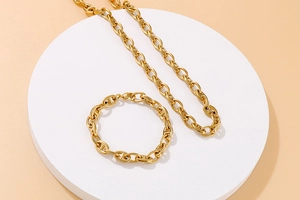 Detail of gold oval link necklace and bracelet set displayed on a minimalist white stand