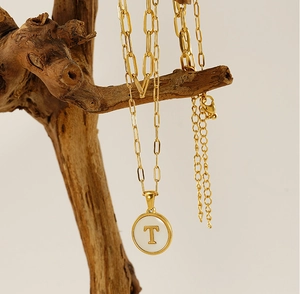 Détail du pendentif doré avec incrustation de nacre et lettre T sur une chaîne trombone