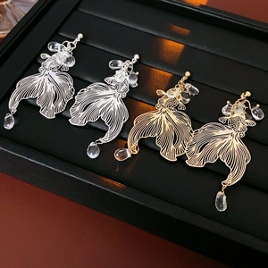 Detailed macro view of gold and silver koi earrings with dangling crystal water drops