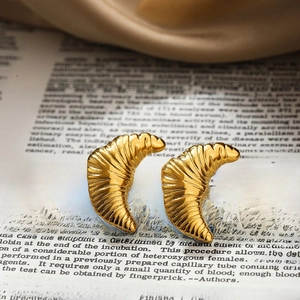Macro detail of 18K gold croissant stud earrings on vintage book and silk background