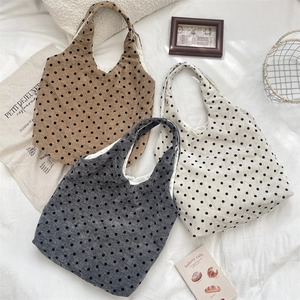 Three minimalist polka dot canvas tote bags in tan, gray and off-white on a fabric background