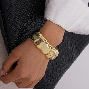 Detailed shot of the gold acrylic cuff bracelet with irregular wavy texture and glossy finish