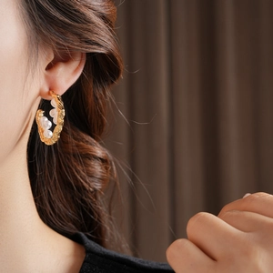 Detail of C-shaped gold twisted hoop earrings with embedded white pearls on a model