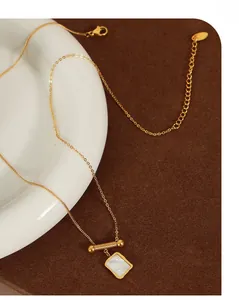 Detailed close-up of a gold necklace with a square white shell pendant and textured cylinder