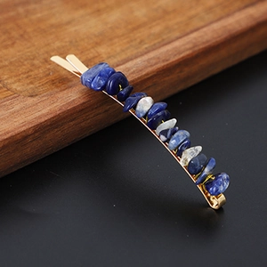 Close-up of golden hair clip with blue and white natural crystal stones on a dark surface