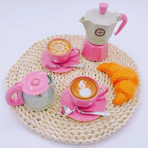 Pink miniature toy coffee set with espresso pot cups and croissant on woven mat