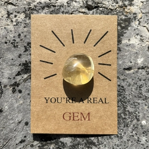 Yellow crystal gemstone on brown gift card with You're a Real Gem text on rock texture