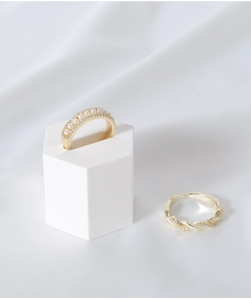 Detailed shot of golden pearl ring and twisted metal band on a white geometric stand