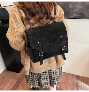 Detail of black suede backpack with dual buckle straps worn over a brown sweater