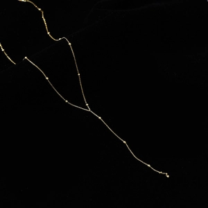 Detail of gold Y-shaped necklace with delicate beaded chain on black velvet