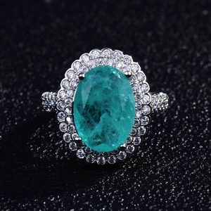 Macro detail of oval Paraiba ring featuring double halo pave setting on black surface