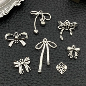 Collection of silver bow and heart alloy charms for DIY jewelry on black leather background