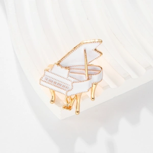 Artistic white enamel piano brooch with gold-plated alloy details on textured background