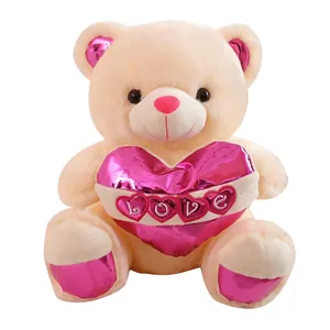 Cream teddy bear plush toy holding a large pink LOVE heart on a clean white background