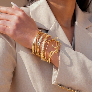 Detail of multi-layered gold irregular geometric twisted bracelets set on model's wrist