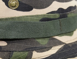 Macro detail of camouflage boonie hat with canvas webbing and metal button buckle