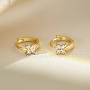 Macro shot of gold floral earrings with clear zircon stones on soft silk fabric