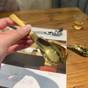 Close-up of hand holding a polished golden stainless steel round dessert spoon