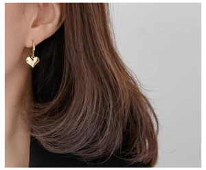 Close-up of elegant gold heart dangle earrings worn by a model in soft lighting