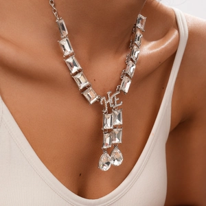 Macro detail of silver geometric crystal necklace with HE letters and drop pendant