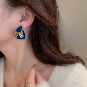 Detail of blue velvet heart earring with gold bow knot on model's earlobe