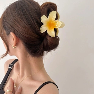 Frangipani flower hair claw clip with yellow gradient finish on casual bun hairstyle