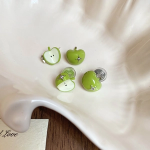 Macro view of green enamel apple stud earrings with sparkling zircon crystals in a shell tray
