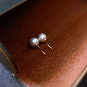 Macro shot of silver pearl stud earrings with gold pins in a wooden container