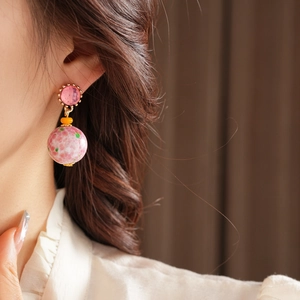 Gros plan de boucles d'oreilles vintage en céramique rose et dorée sur un mannequin