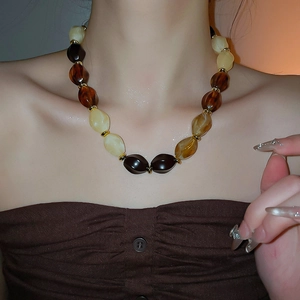 Close-up of retro acrylic bead necklace with amber tones and gold spacers on model
