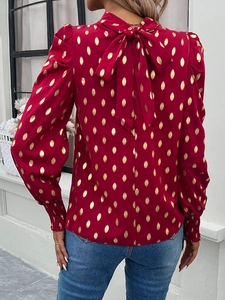 Detail view of red blouse with gold polka dots and a back bow tie at the neckline