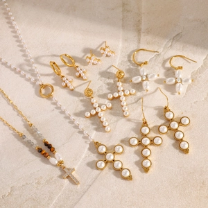 Elegant gold pearl cross jewelry set with layered necklaces and earrings on stone surface